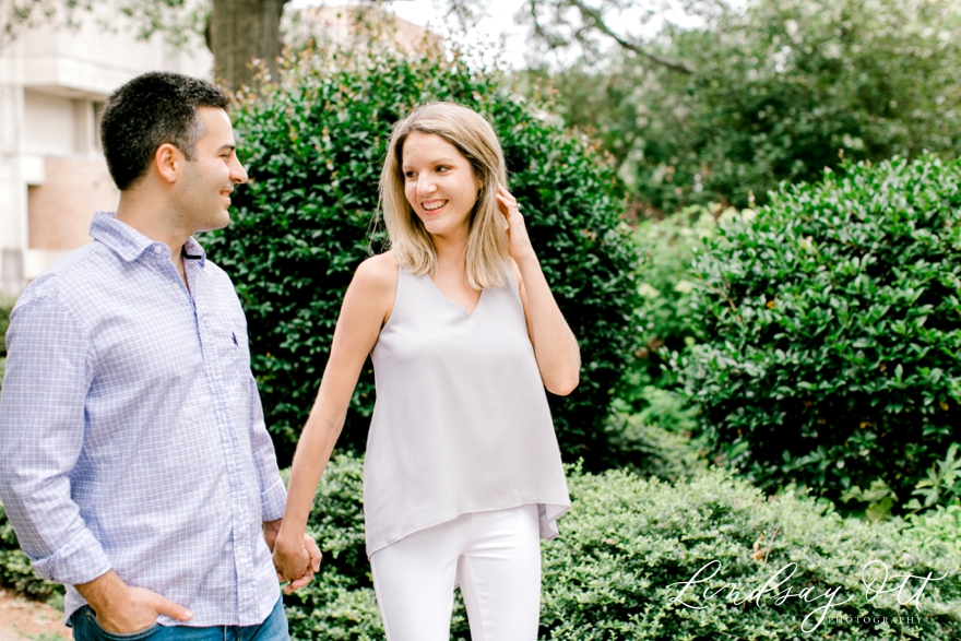 Engagement session couple walking together holding hands and looking at each other with greenery behind them